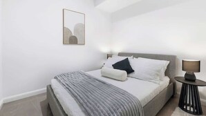 A modern bedroom with a bed, bedside lamps, and a framed artwork on the wall. - Lvl50 Ocean Views | 3BR Skyhome | Pool+Gym+Parking (Surfers Paradise)