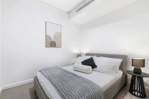 A modern bedroom with a bed, bedside lamps, and a framed artwork on the wall. - Lvl50 Ocean Views | 3BR Skyhome | Pool+Gym+Parking (Surfers Paradise)