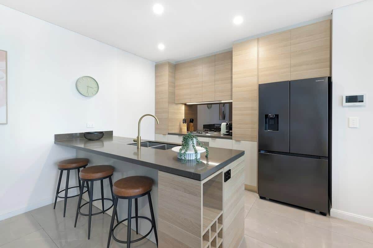 Una cocina moderna con una isla central, taburetes de bar, un refrigerador negro y un reloj en la pared.