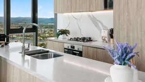 A modern kitchen with a large window, a sink, a stove, and a potted plant. - Lvl 36 Ocean Views | 2BR skyhome | sky pool (Broadbeach)