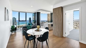 A modern living space with a dining area, a kitchen, and a balcony with a city view. - Lvl 36 Ocean Views | 2BR skyhome | sky pool (Broadbeach)