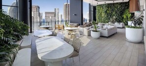Eine Dachterrasse mit Außenmöbeln, Blick auf die Stadtlandschaft und einer grünen Wand.