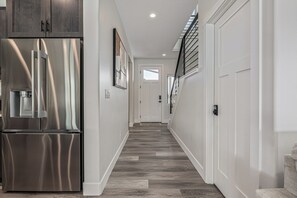A modern kitchen with a stainless steel refrigerator and a water dispenser, a hallway with a wooden floor, and a staircase with a metal railing.