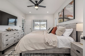 Un dormitorio con cama, cómoda, ventilador de techo y cuadros en la pared.