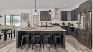 A modern kitchen with dark cabinets, a large island, bar stools, and a stainless steel refrigerator.