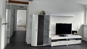 Una sala de estar moderna con un televisor de pantalla plana, un aparador de vidrio y una viga de techo de madera.