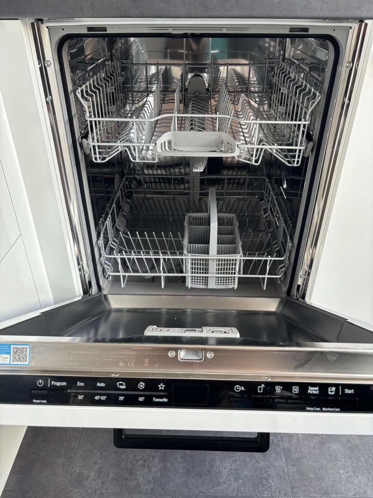 An empty dishwasher with multiple racks and a control panel with various settings.