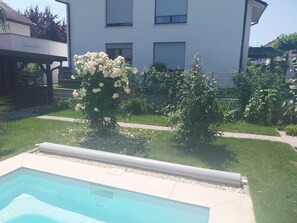 En swimmingpool med ett klart, blått vatten, omgiven av en välskött gräsmatta och en mängd olika blommande växter.