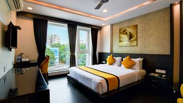 Habitación de hotel con cama, mesita de noche, escritorio, silla, ventilador de techo y ventana con cortinas.
