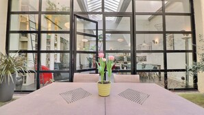Ein Tisch mit einem gelben Blumentopf, große Fenster und Blick ins Innere.