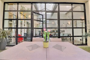 Ein Tisch mit einem gelben Blumentopf, große Fenster und Blick ins Innere.