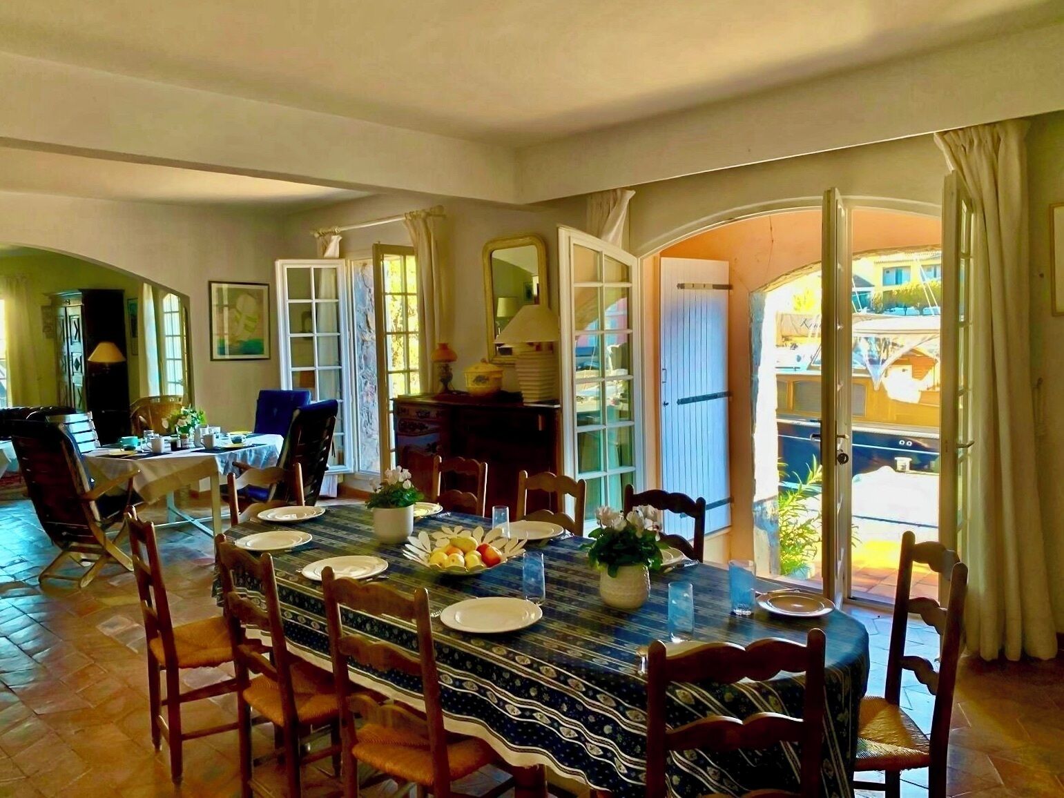 A dining area with a table set for four, surrounded by chairs, with a view of the outside through open doors.