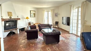Un salón con chimenea, sofás de cuero, televisor y ventanas grandes.