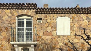 Un edificio de piedra con un balcón, una entrada portonada y un pequeño jardín.