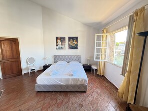 A bedroom with a bed, a wooden door, a window with curtains, and two wall-mounted pictures.