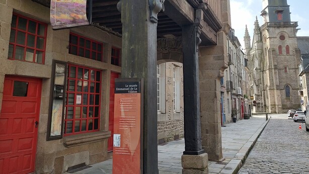 A historic building with a red door, a banner, and a sign indicating a museum.