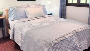 A neatly arranged bedroom with a bed, a nightstand, a lamp, a framed picture on the wall, and a window with curtains.