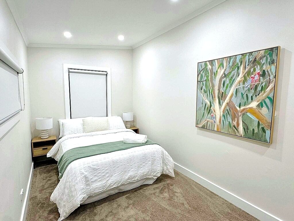 Un dormitorio con una cama, una mesita de noche, un cuadro colgado en la pared y una ventana.