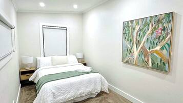 Un dormitorio con una cama, una mesita de noche, un cuadro colgado en la pared y una ventana.