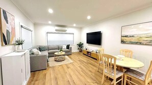 A living room with a sofa, a coffee table, a TV, and a dining table with chairs.