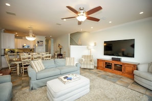 A living room with a sofa, ottoman, TV, and a ceiling fan. - Sea Suite Pensacola Beach Condo (Gulf Breeze)