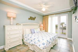 A bedroom with a bed, dresser, ceiling fan, and a view through the door. - Sea Suite Pensacola Beach Condo (Gulf Breeze)
