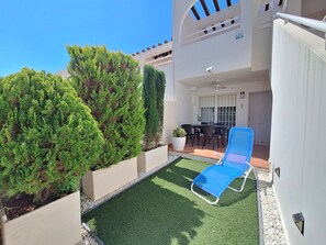 Ein Balkon mit Kunstgrasanlage, einem blauen Liegestuhl und Topfpflanzen.