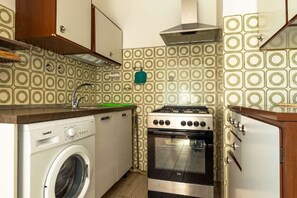 A compact kitchen with a washing machine, oven, and a tiled backsplash.