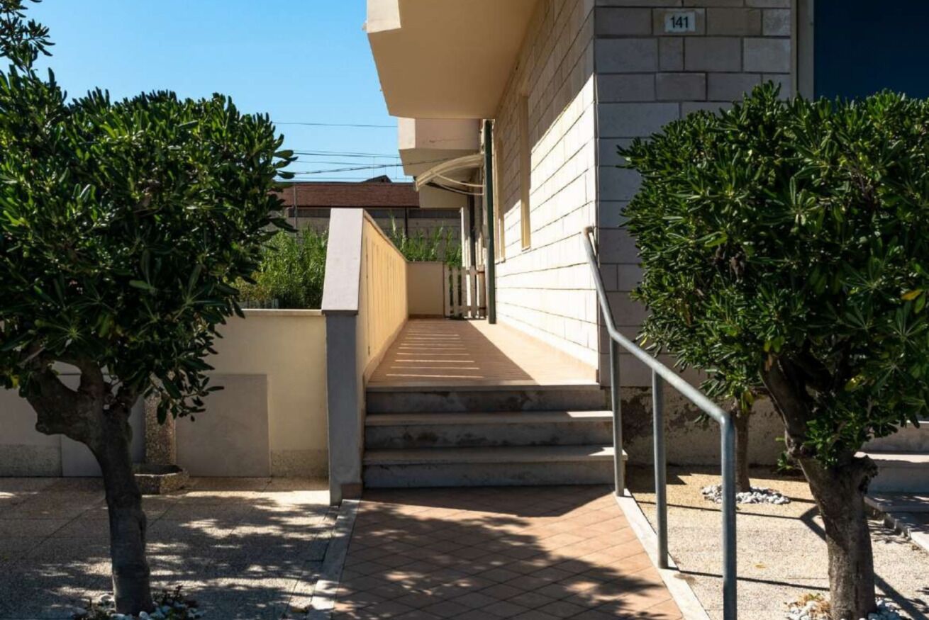 A building with a staircase leading to a landing, surrounded by trees and a clear sky.