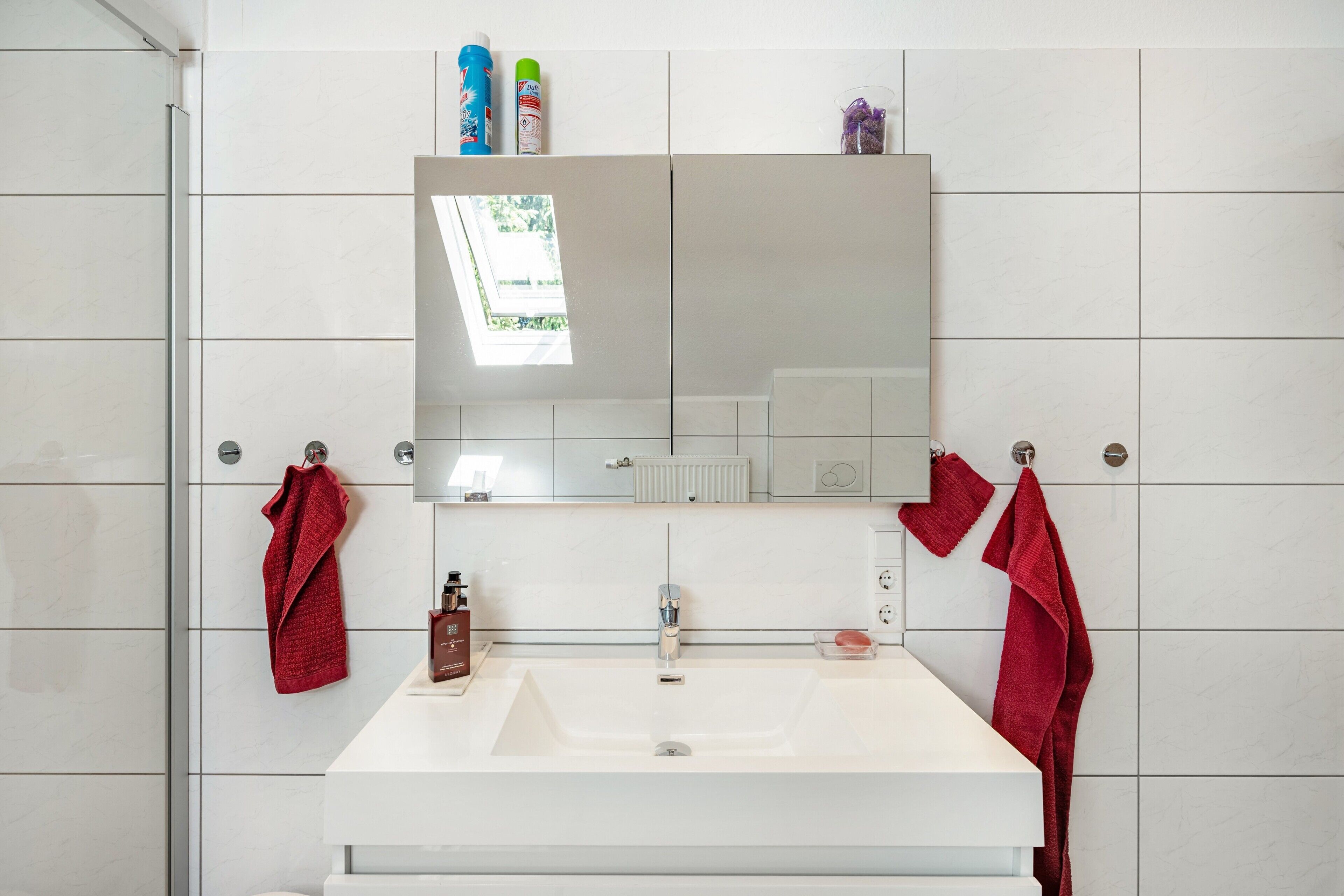 A bathroom with a white sink, a mirror, and two red towels hanging on towel bars.