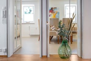 A room with a wooden floor, a green vase with dried plants, a white door, and a dining area with chairs and a table in the background. - Bächle Lodge with 3 Bedrooms and Mountain Views in the Heart of Hornberg (Hornberg)