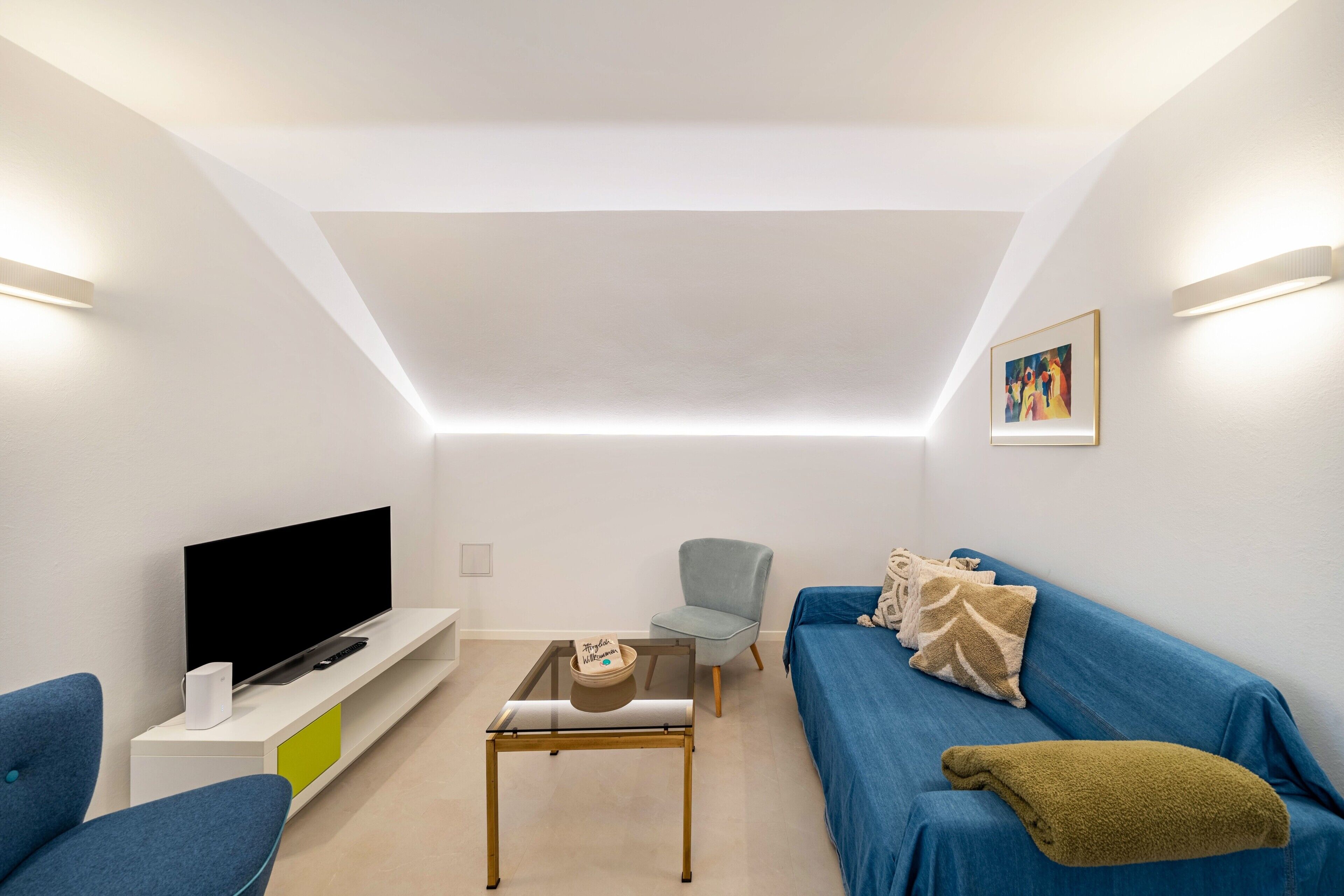 Ein modernes Wohnzimmer mit Flachbildfernseher, Sofa, Couchtisch und Sessel.