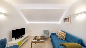 Ein modernes Wohnzimmer mit Flachbildfernseher, Sofa, Couchtisch und Sessel.