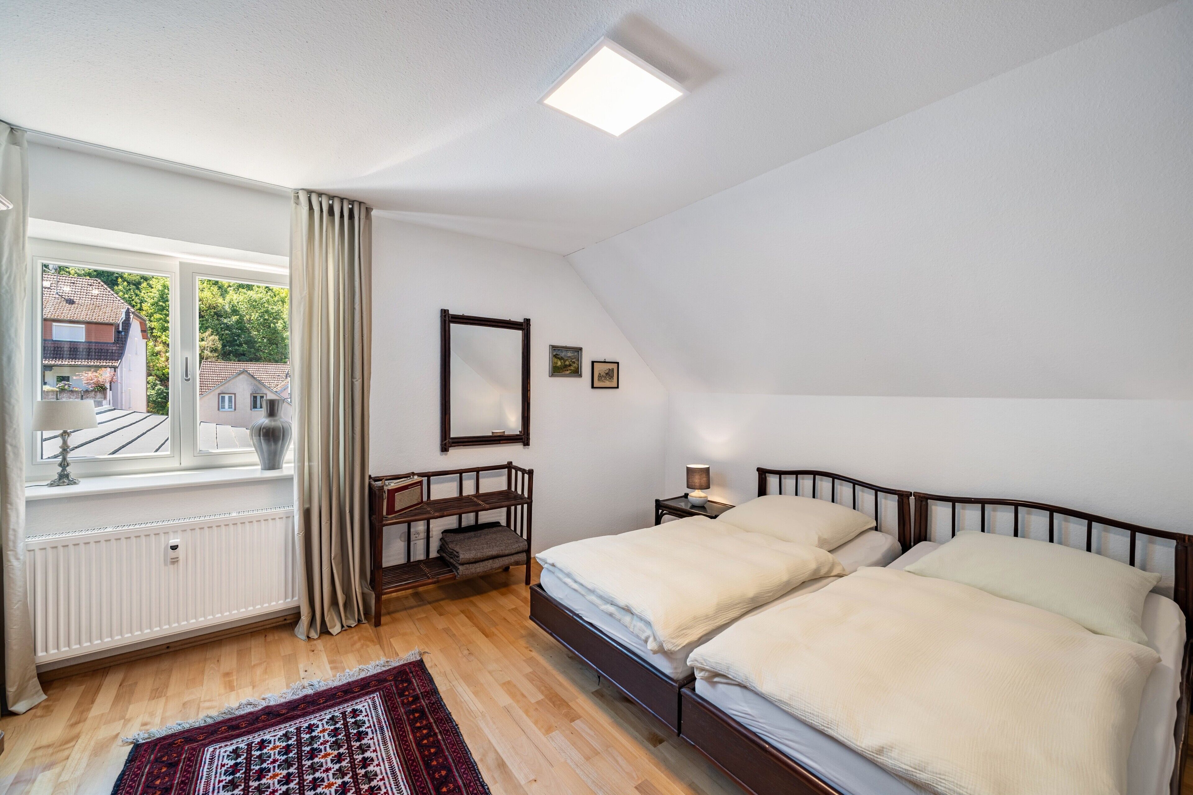 Une chambre à coucher comprenant un lit, une table de chevet, un miroir, une fenêtre avec des rideaux et un radiateur.