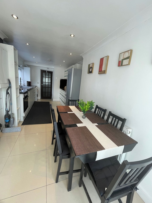 A dining area with a long table, chairs, and a kitchen in the background.