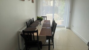 Un comedor con una mesa dispuesta para seis personas, rodeada de sillas, una estufa en la pared y una ventana con cortinas.