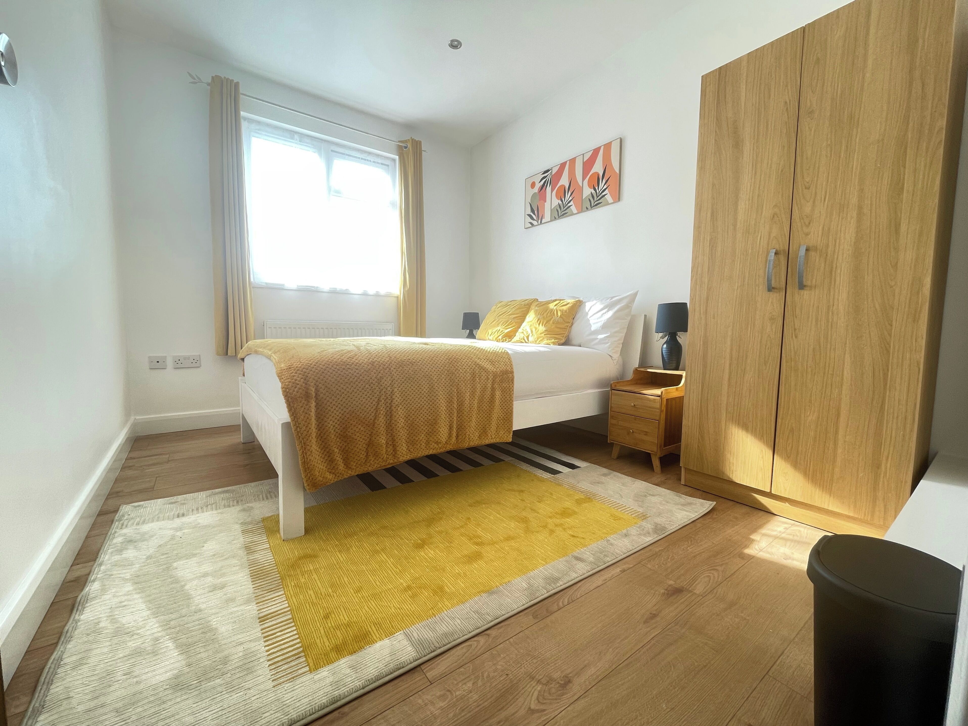 A bedroom with a bed, bedside table, lamp, wardrobe, and a window with curtains.