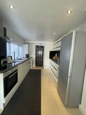 A modern kitchen with a stainless steel refrigerator, a built-in oven, and a black countertop. - Tottenham - Sleeps 10 - Garden - Near Transport (London)