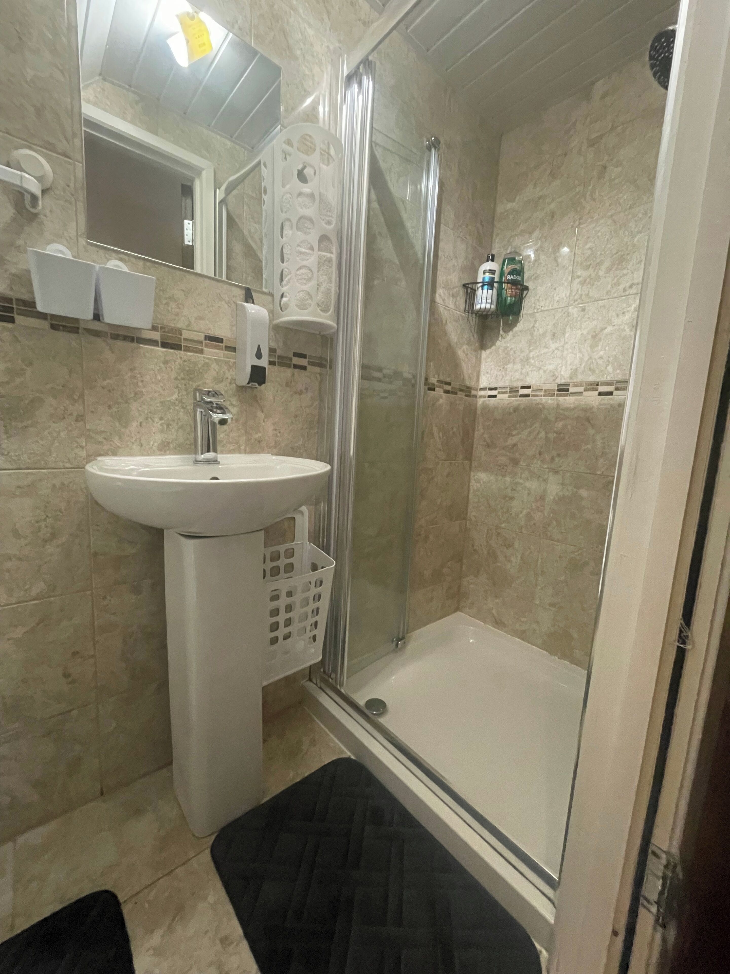 Un baño con lavamanos, espejo, ducha y artículos de aseo.