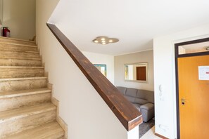 A staircase with wooden steps and a wooden handrail, leading to a room with a gray sofa and a door with a light switch. - Modern apartment 1, 5M Montepulciano with parking (Toscana)