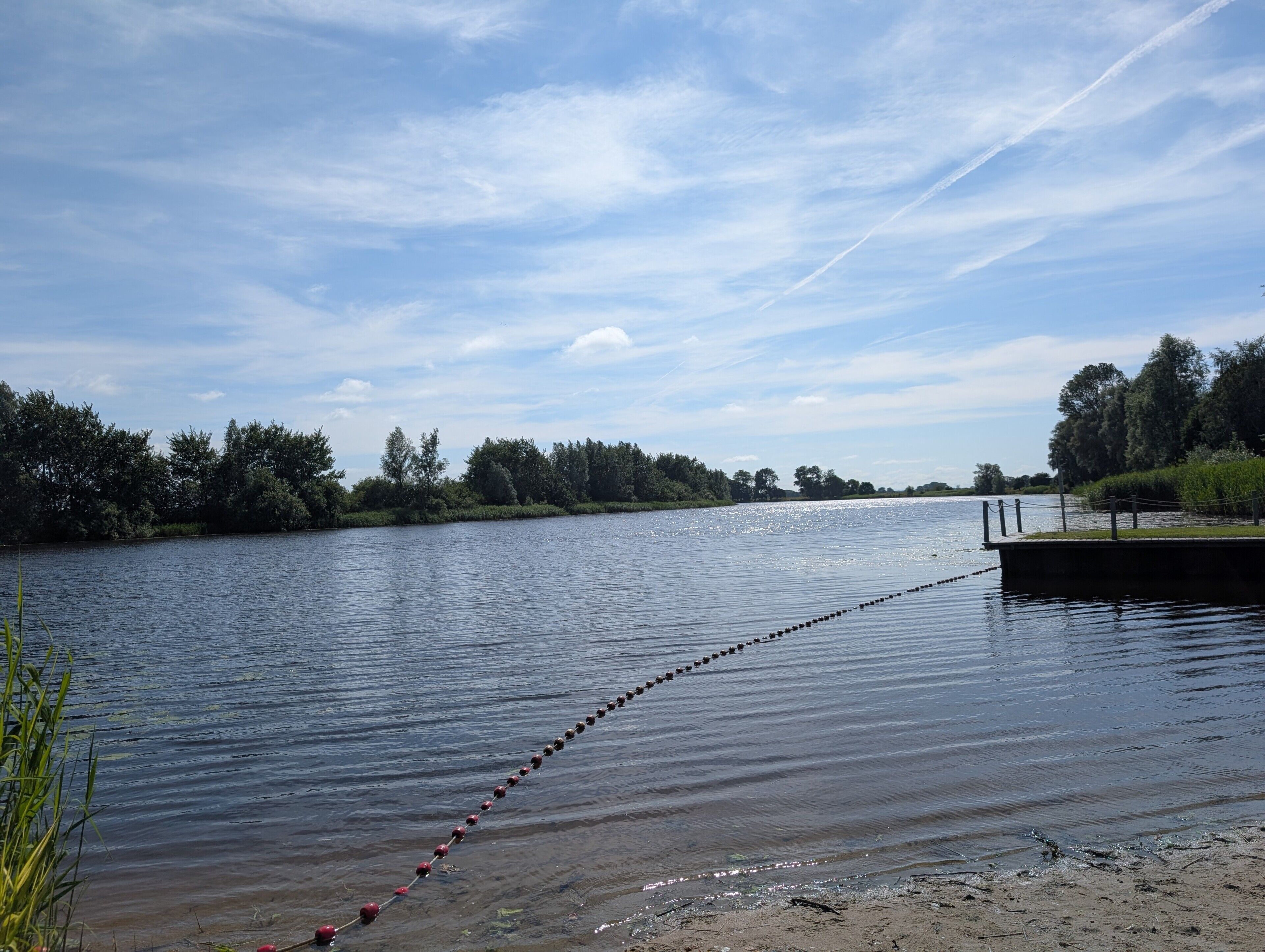 A calm river with a dock extending into the water, surrounded by trees and a clear sky.