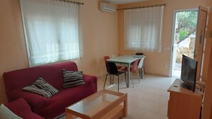 A living room with a red sofa, a wooden coffee table, a dining table with chairs, and a television on a wooden stand. - Central house with private pool - 4 guests (Mont-roig del Camp)