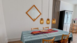 Uma sala de jantar com mesa posta para quatro, cadeiras de madeira, toalha de mesa listrada, luminárias pendentes, um espelho e um armário.
