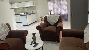 Ein Wohnzimmer mit braunen Sofas, einem kleinen weißen Tisch und einer Küche im Hintergrund.