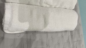 Ein ordentlich gefaltetes weißes Handtuch auf einem Bett mit einem gemusterten Bettbezug.