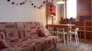 Un salon chaleureux avec un canapé, une table à manger, des chaises et un coin cuisine doté de meubles en bois et d’une fenêtre.