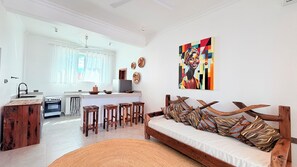 A modern kitchen with a dining area, a sofa with patterned cushions, and a painting on the wall. - Zanziland Apartments (Kiwengwa)