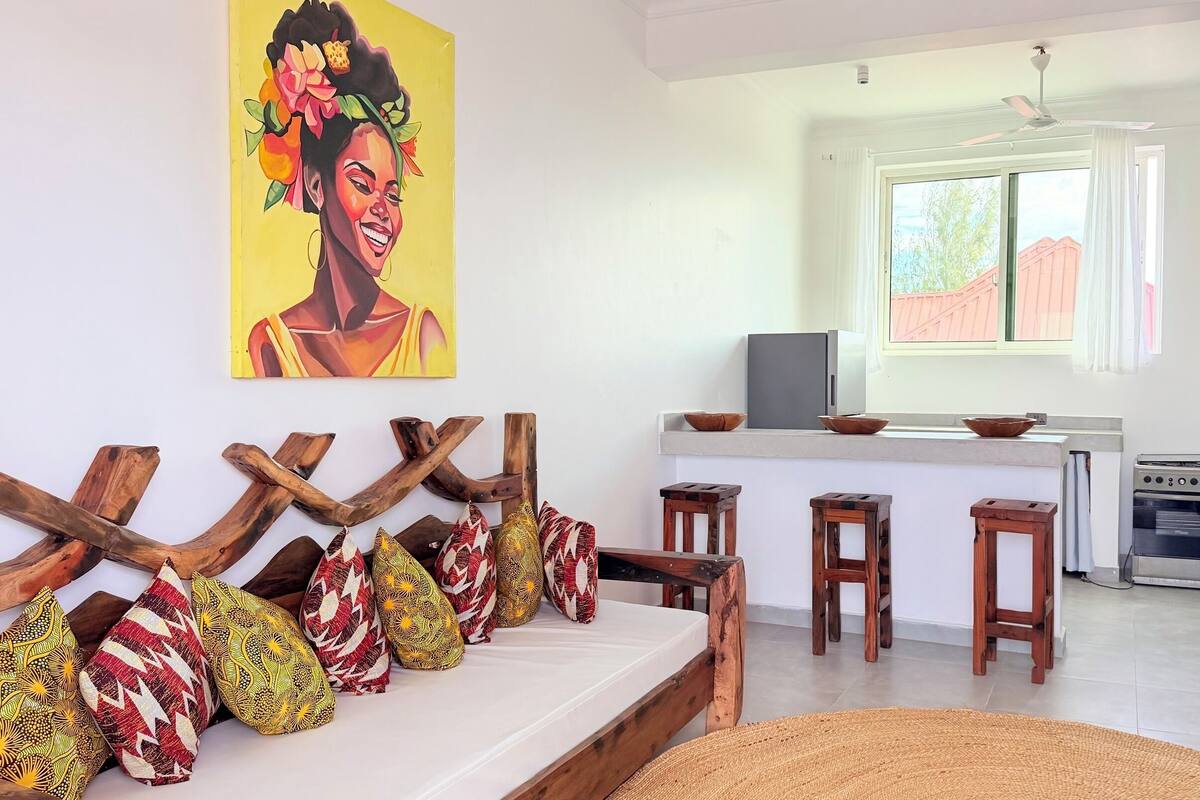 A modern kitchen with a built-in oven and microwave, a dining area with a bench and stools, and a large window providing natural light.
