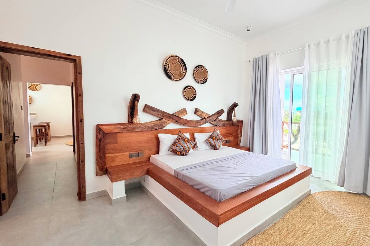 A bedroom with a wooden headboard, a bed with patterned pillows, and a view through a sliding glass door.