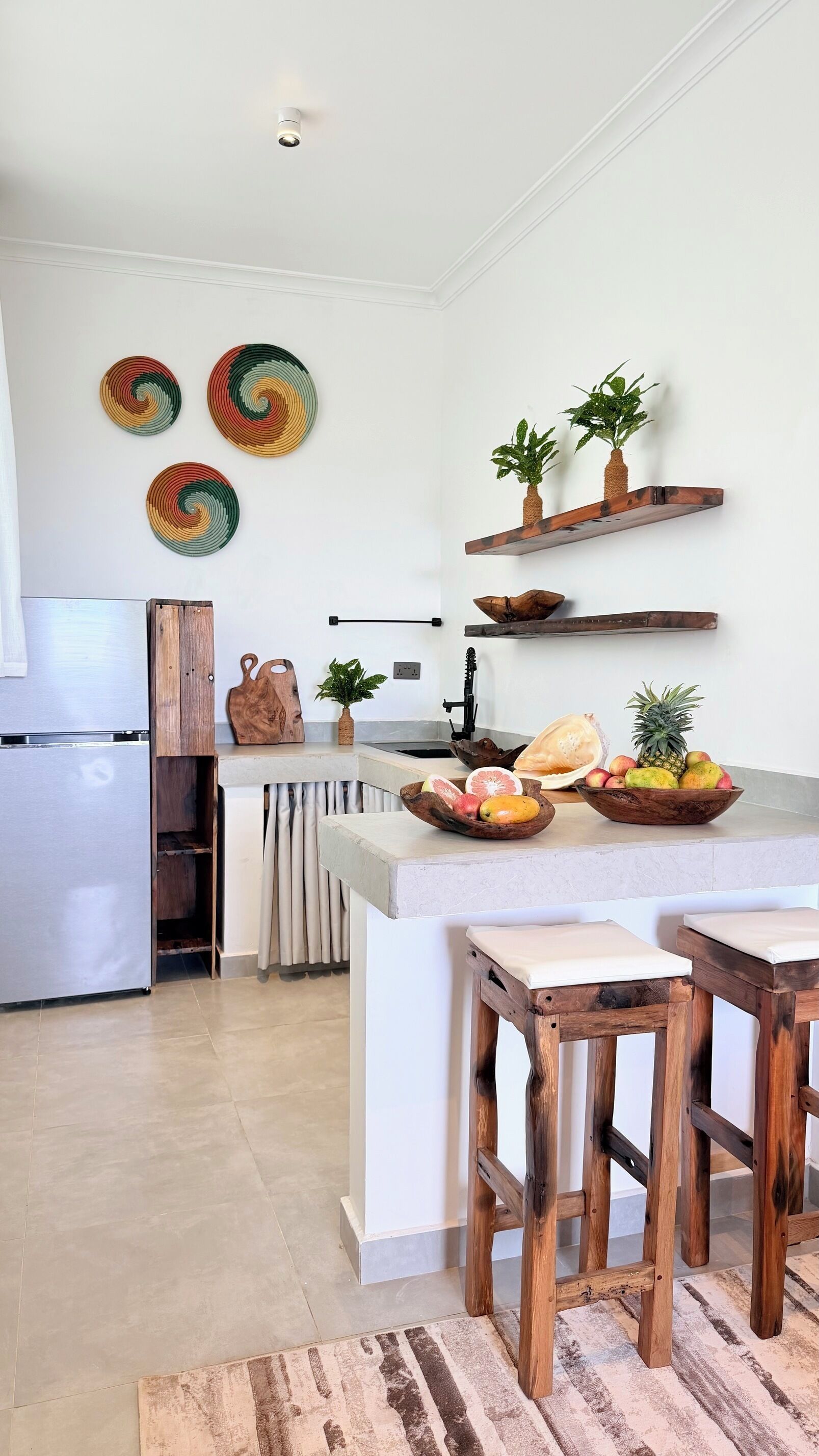 A modern kitchen with a central island, wooden stools, and decorative plates on the wall.